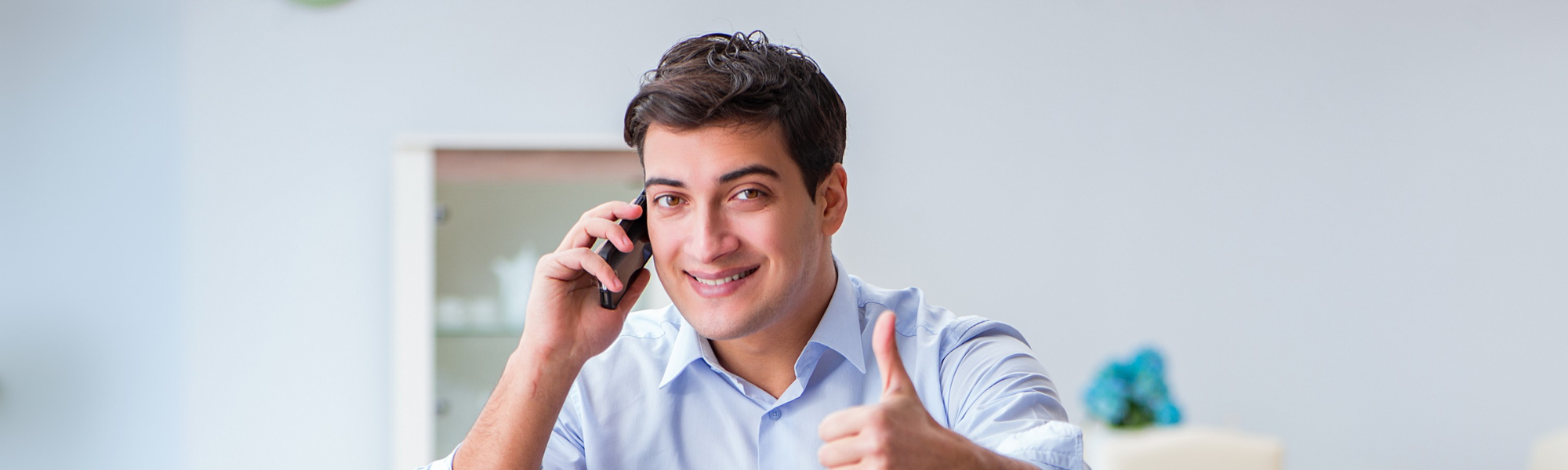 Smiling businessman giving a thumbs-up while talking on the phone, symbolising customer satisfaction, support, and positive business communication.