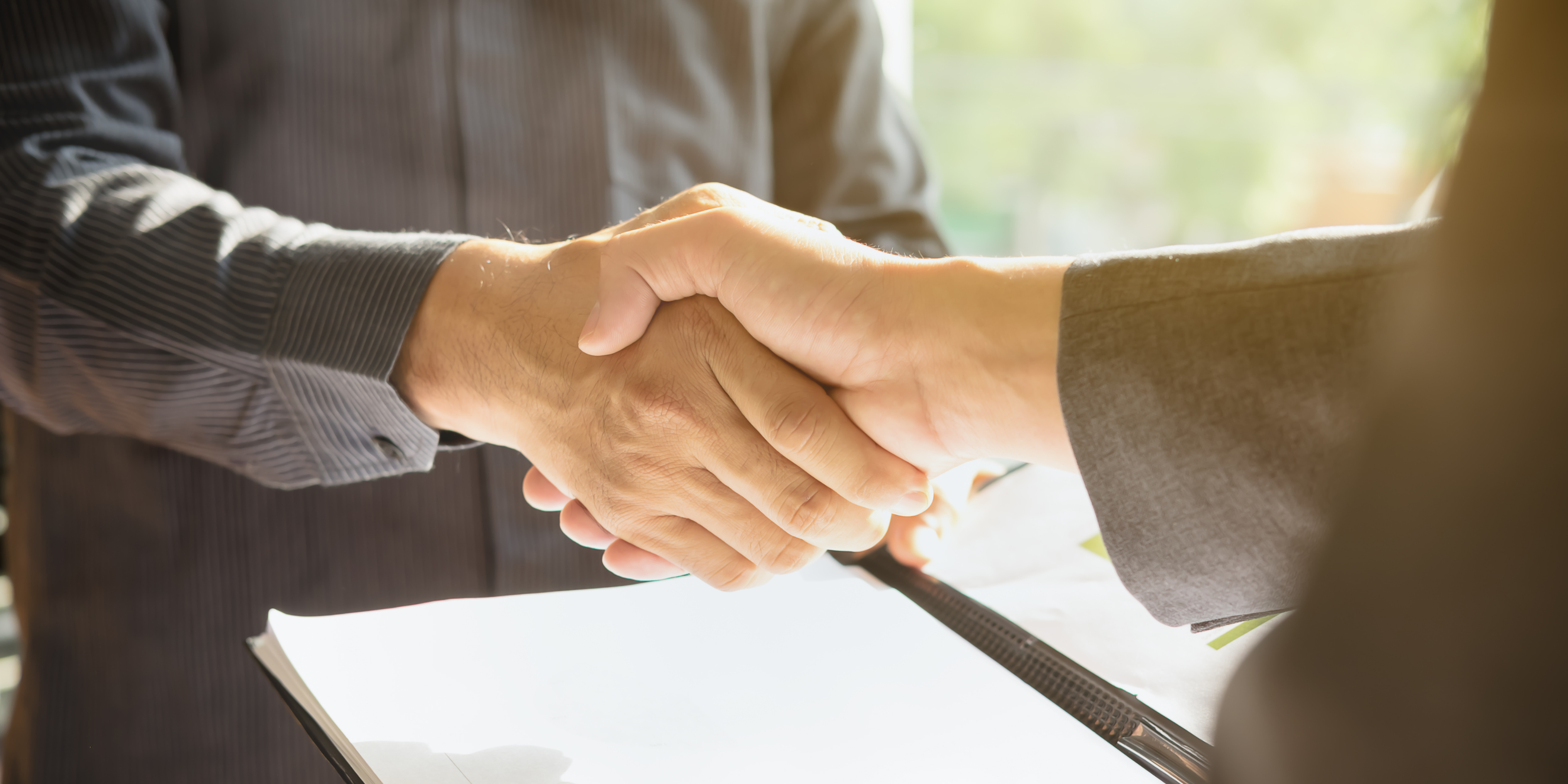 Close-up of two business professionals shaking hands over a contract, symbolising a successful business deal, acquisition, or business sale.