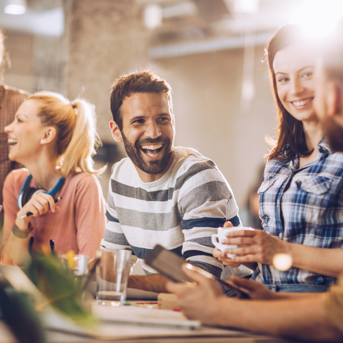 Group of smiling young professionals in a bright, modern office sharing ideas and enjoying a relaxed conversation—capturing collaboration, creativity, and a positive team culture.