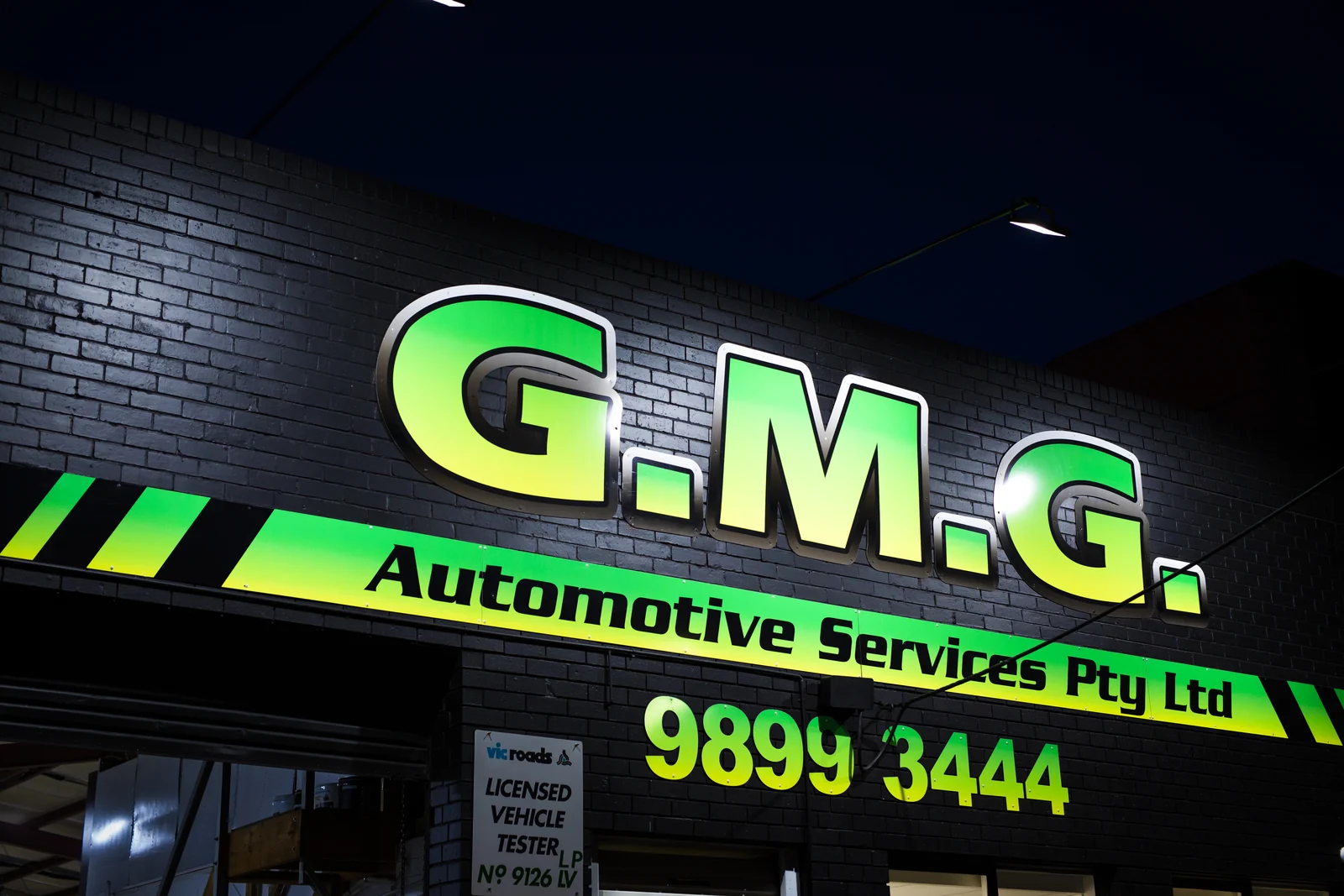 The illuminated GMG Automotive Services sign above the Box Hill workshop at night