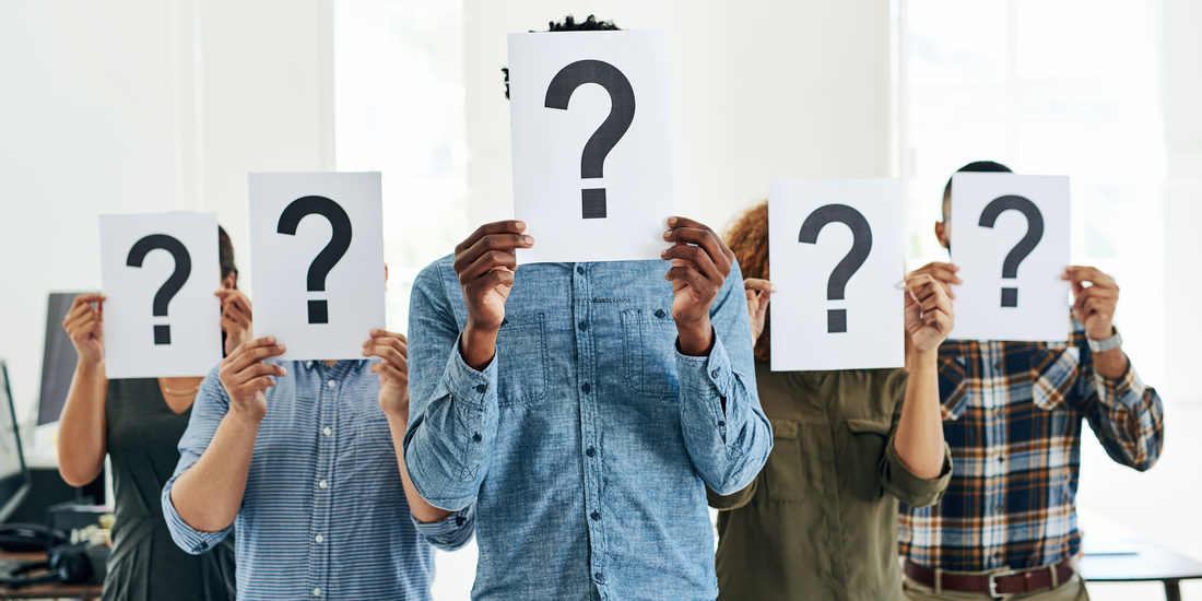A group of people standing in a row, each holding a sheet of paper with a large question mark in front of their face, symbolising confusion or uncertainty.